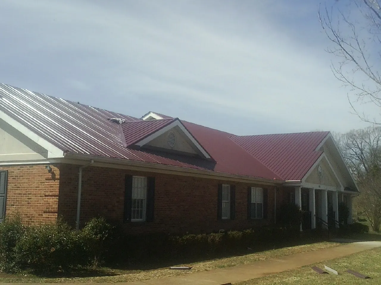 Red metal roof with gabled entries on a long brick building, from a Hail Damage Roof Repair job in Willet