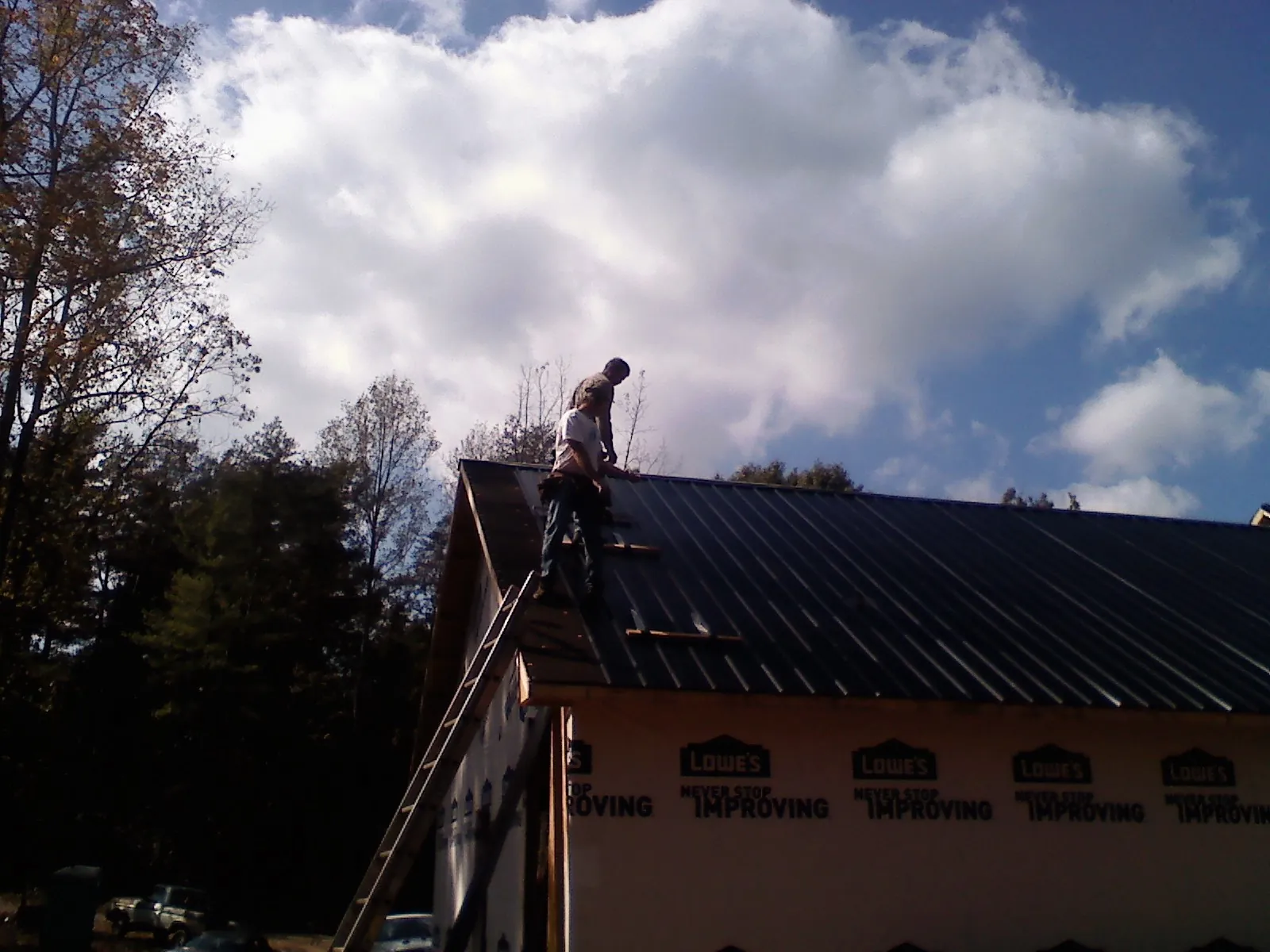 Roofer fastening dark metal panels high against a cloudy sky, from a Roof Inspection job in Willet