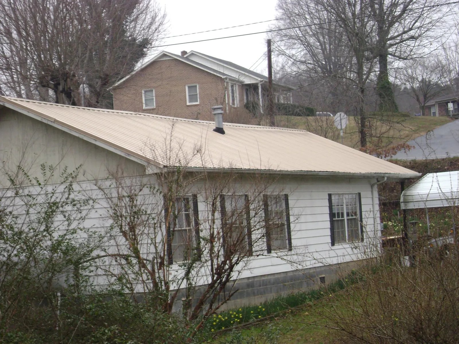 Tan metal roof on a white sided house set into a hillside — Commercial Roofing by Roofing Brothers in Willet